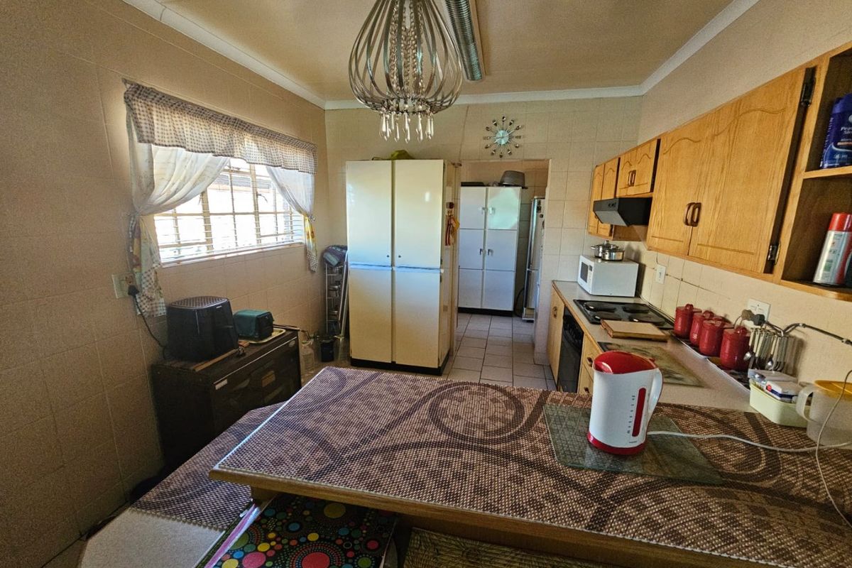 A functional kitchen featuring wooden cabinetry, tiled walls, and a breakfast counter, with an adjacent scullery area visible.