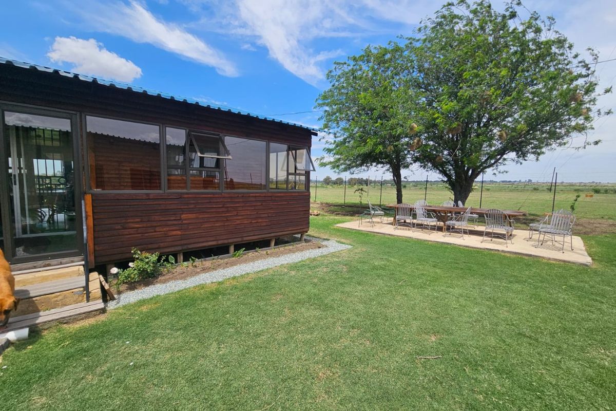 A view of the rear exterior of the timber-clad dwelling, featuring a landscaped lawn, paved patio area, and expansive rural surroundings.