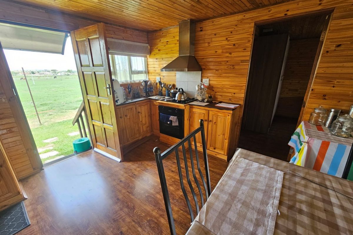 Compact kitchen featuring timber wall paneling, built-in cabinetry, stainless steel extractor fan, and direct access to the outdoor area.