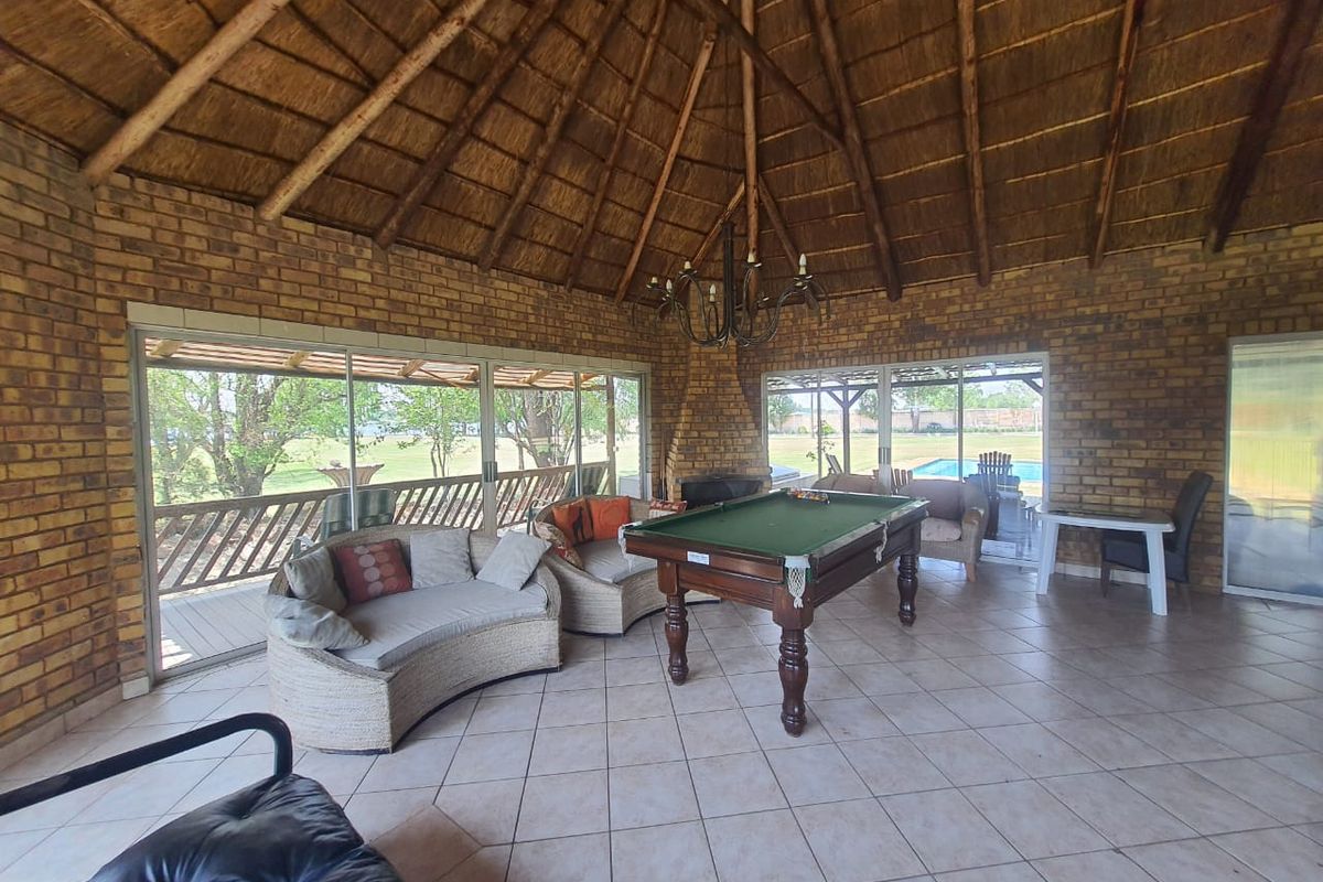 Spacious entertainment area featuring a high thatched roof, exposed brick walls, tiled flooring, and large sliding glass doors opening to the garden and pool.