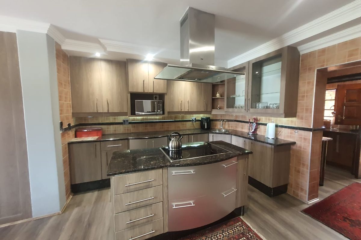 Modern kitchen featuring a central island with a built-in hob, stainless steel extractor fan, granite countertops, and ample wooden cabinetry.