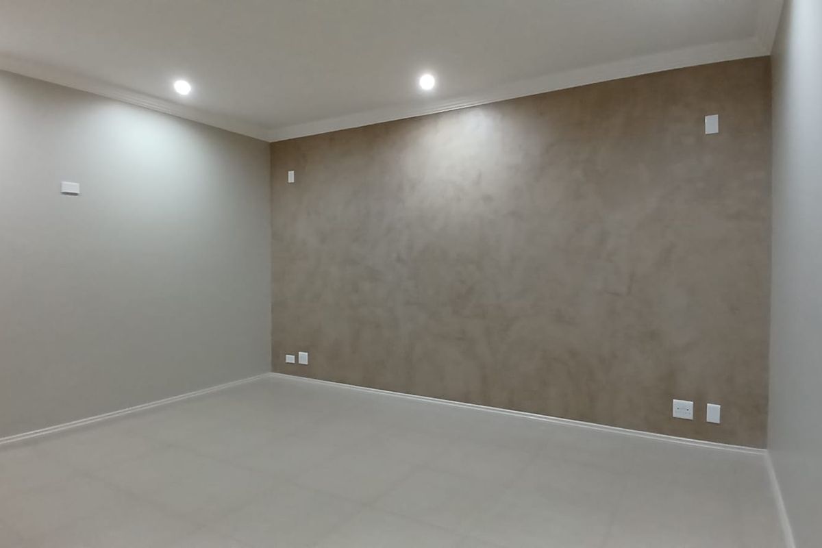 A spacious, empty living room featuring neutral tiled flooring, recessed ceiling lighting, and a decorative textured feature wall.
