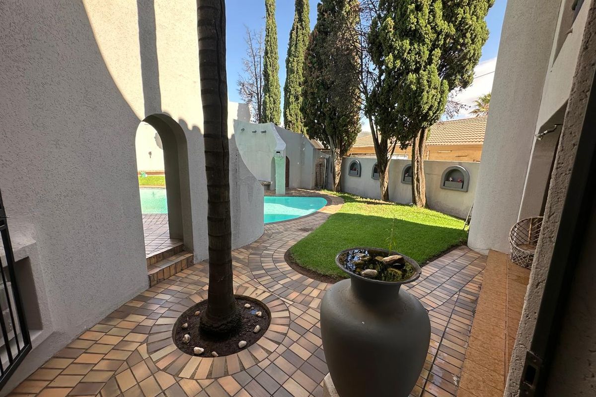A private courtyard area featuring paved walkways, a manicured lawn, and direct access to a swimming pool, framed by architectural archways.