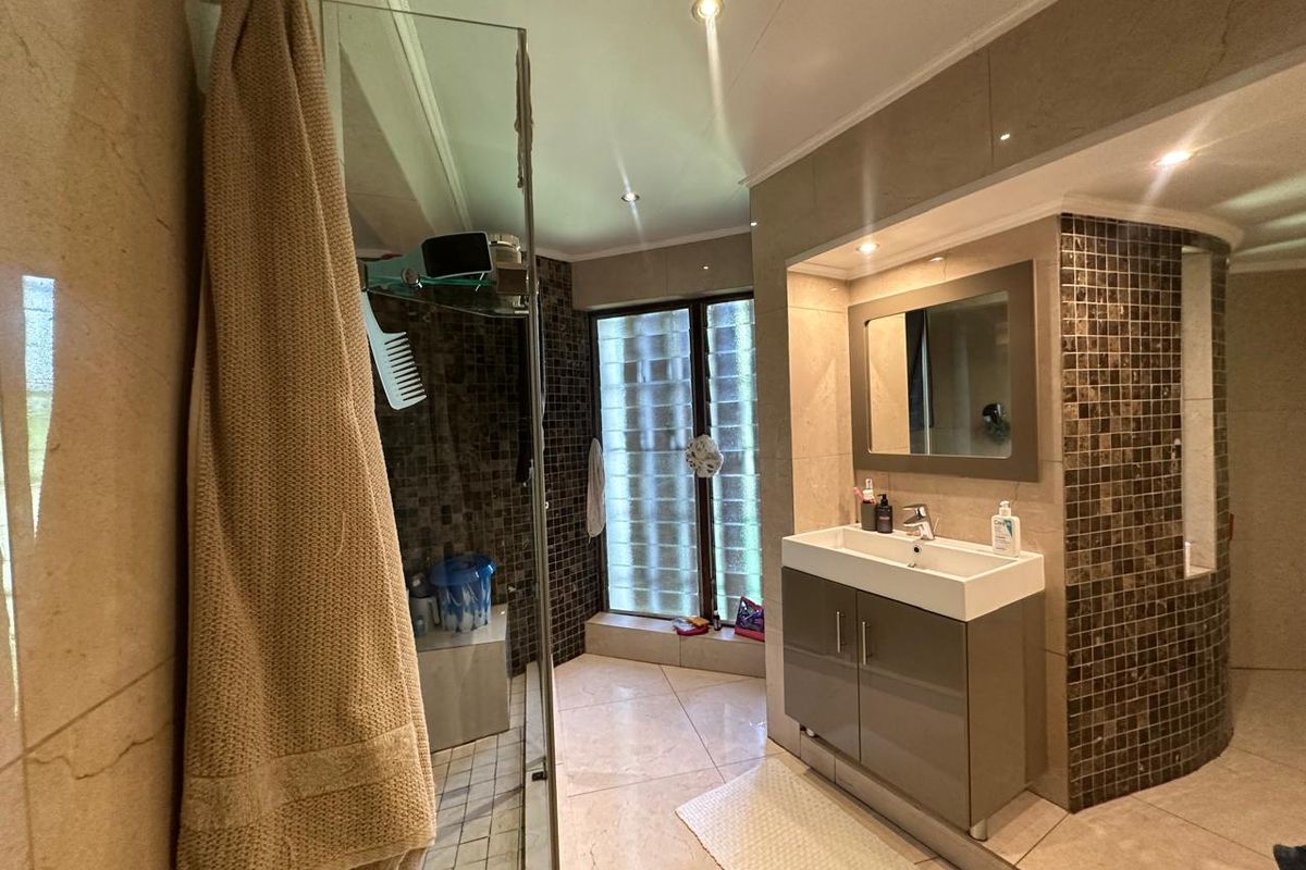Modern bathroom featuring a glass-enclosed shower, vanity with integrated basin, and decorative mosaic tile accents with glass block window detailing.