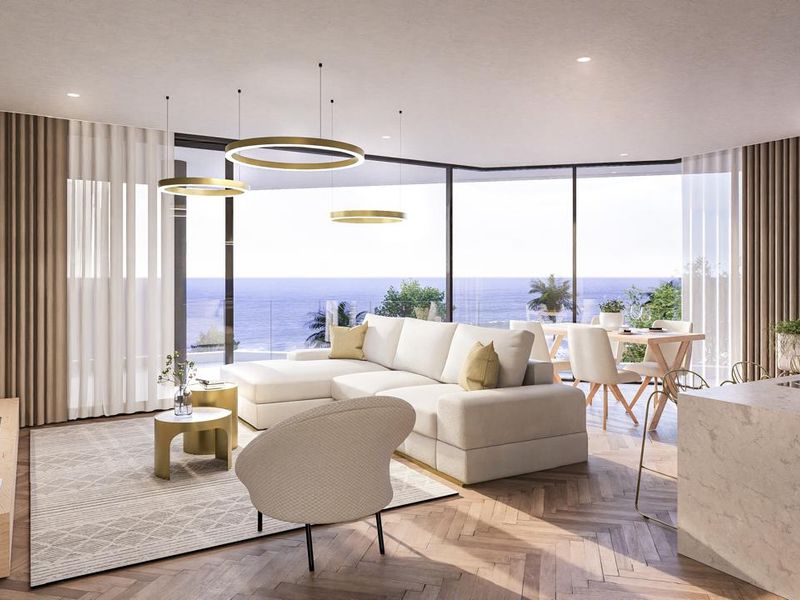 A modern open-plan living and dining area featuring floor-to-ceiling glass windows with expansive ocean views, herringbone timber flooring, and recessed ceiling lighting.