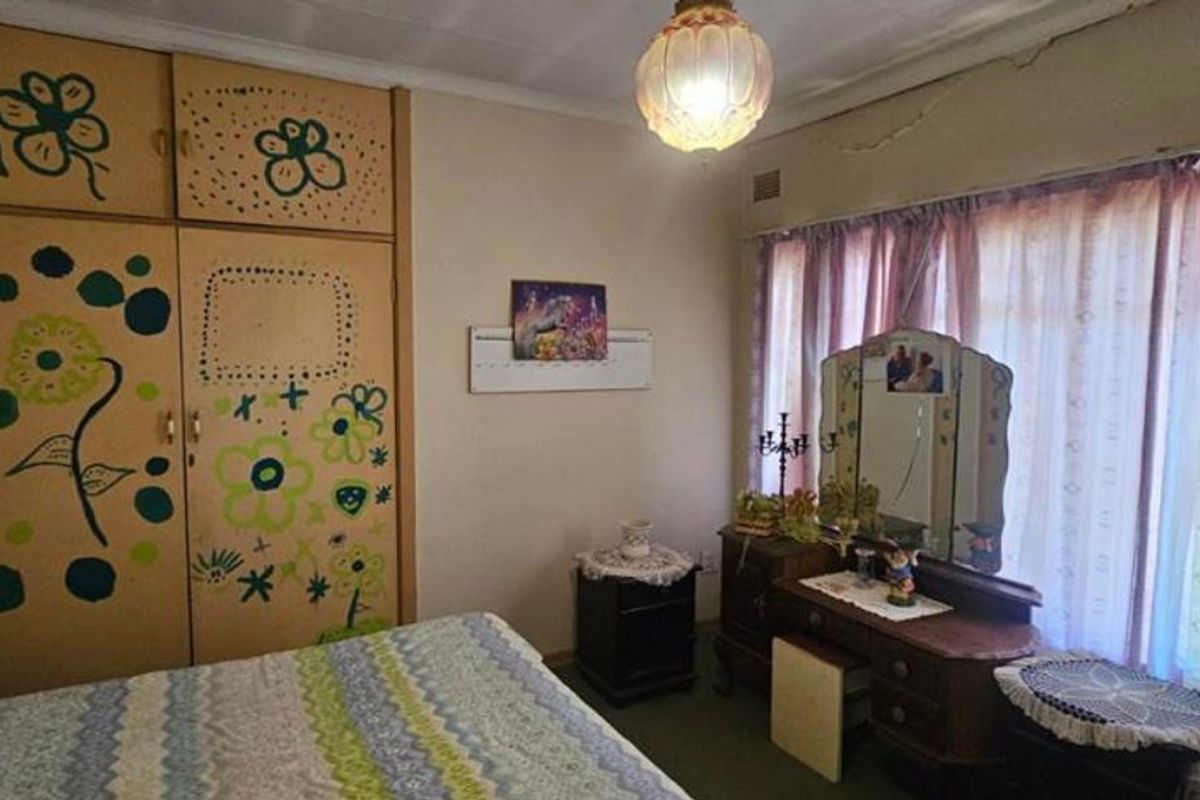 A bedroom featuring built-in wooden cupboards and large windows with curtains, requiring cosmetic updates to modernize the space.