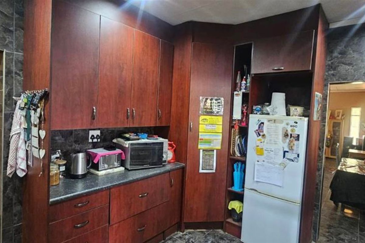 A kitchen area featuring dark wood cabinetry, stone-look wall tiling, and a dedicated space for a refrigerator.