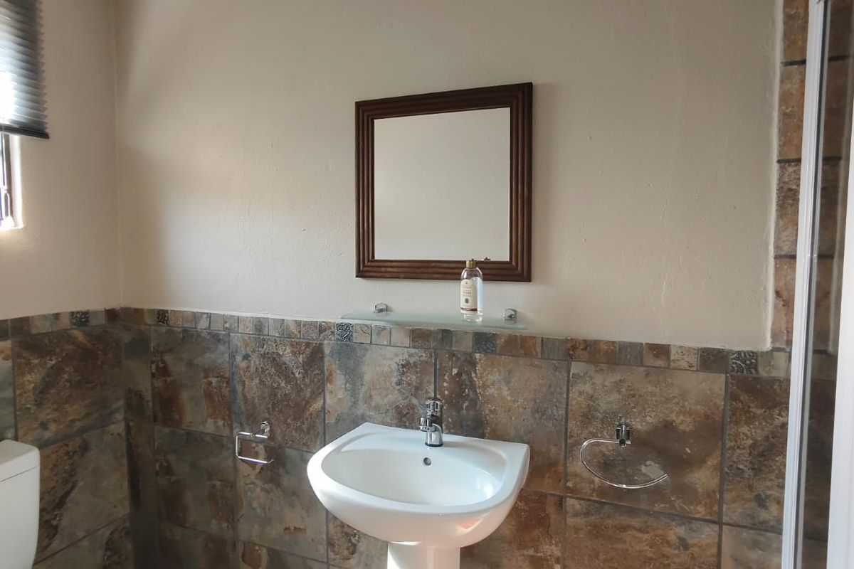 A functional bathroom featuring a pedestal basin, wall-mounted mirror, and natural stone-look wall and floor tiling.