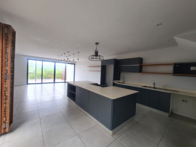 Spacious open-plan kitchen and living area featuring modern dark cabinetry, stone countertops, a central island, and large sliding doors leading to an outdoor space.