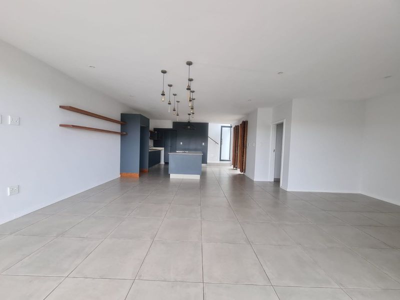 Spacious open-plan living and kitchen area featuring modern dark cabinetry, a central island, tiled flooring, and contemporary pendant lighting.