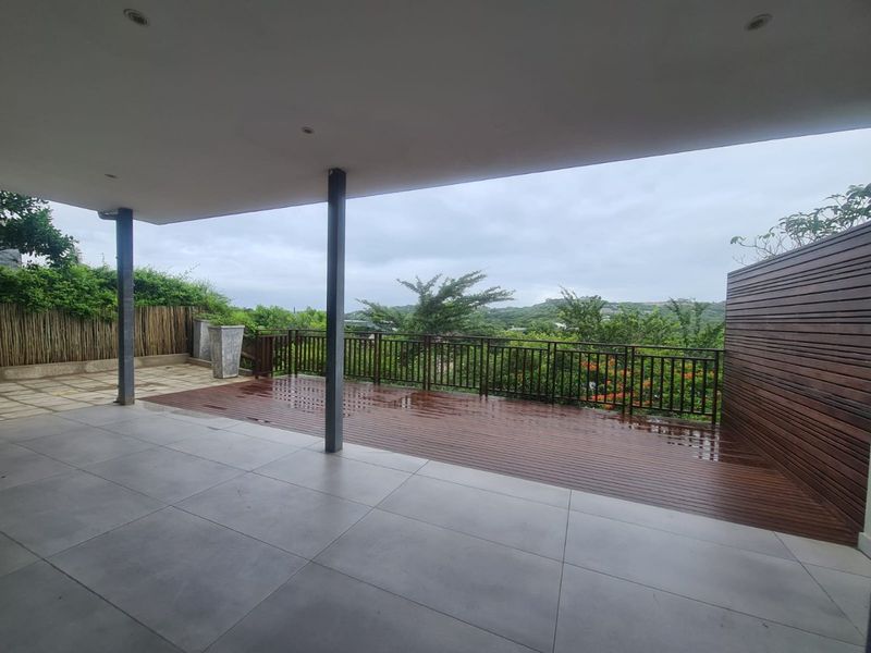 Spacious covered patio featuring a combination of tiled flooring and timber decking, with a metal balustrade and scenic outdoor views.