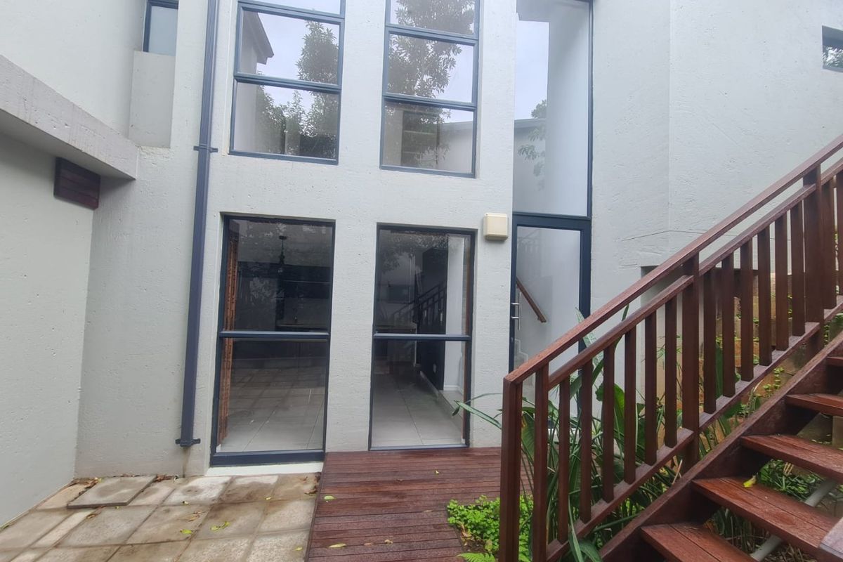 Rear exterior view featuring a timber deck, wooden staircase with handrail, and large floor-to-ceiling windows providing natural light to the interior.