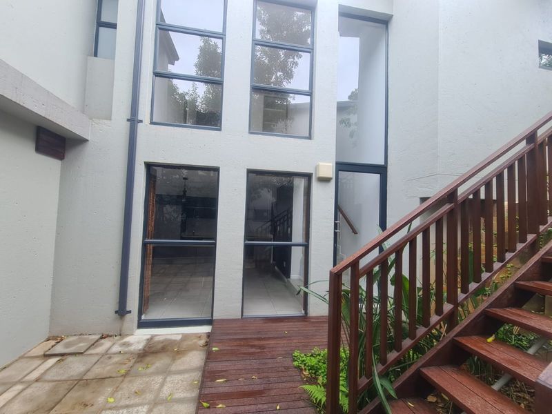 Rear exterior view featuring a timber deck, wooden staircase with handrail, and large floor-to-ceiling windows providing natural light to the interior.