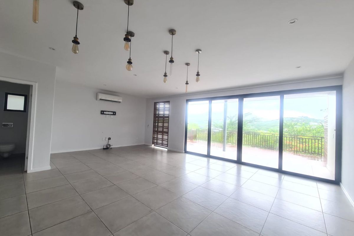 Spacious, light-filled living area featuring large sliding glass doors, neutral tiled flooring, and modern pendant lighting, with direct access to an outdoor balcony.