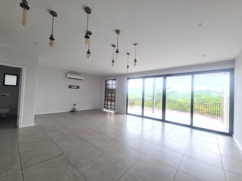 Spacious, light-filled living area featuring large sliding glass doors, neutral tiled flooring, and modern pendant lighting, with direct access to an outdoor balcony.