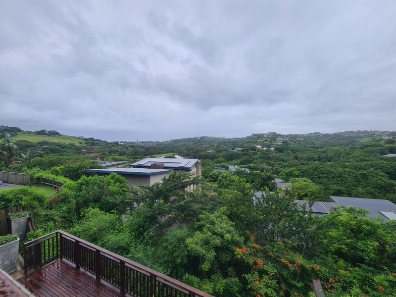 Elevated view overlooking a lush green landscape and surrounding residential properties, featuring a wooden deck with a safety railing in the foreground.