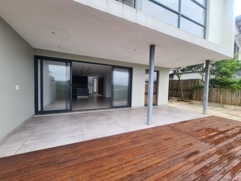 Covered patio area featuring large sliding glass doors, tiled flooring, and timber decking, providing a seamless transition to the interior living space.