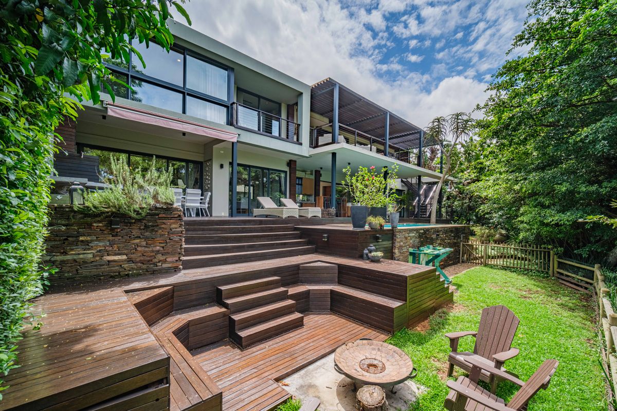 Spacious multi-level rear garden featuring extensive timber decking, a swimming pool, stone retaining walls, and a large balcony overlooking the landscaped yard.