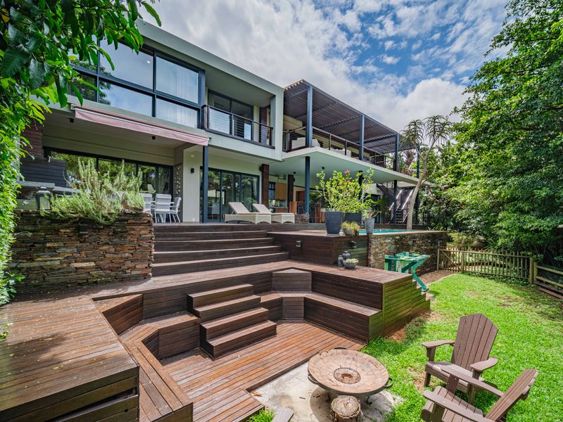 Spacious multi-level rear garden featuring extensive timber decking, a swimming pool, stone retaining walls, and a large balcony overlooking the landscaped yard.