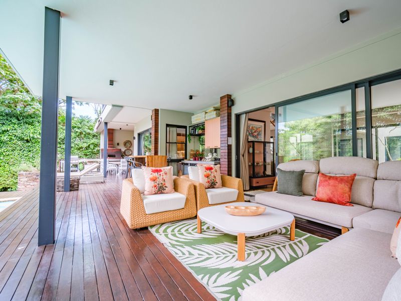 Spacious covered patio featuring timber decking, built-in braai area, and seamless flow to the pool area through large sliding glass doors.