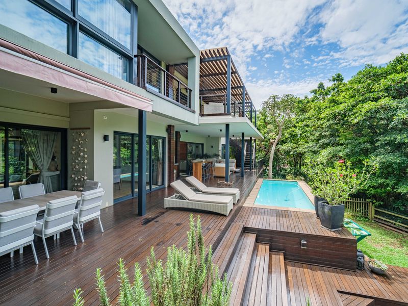 Spacious rear exterior featuring a large timber deck, swimming pool, covered patio area, and balcony overlooking a lush garden setting.