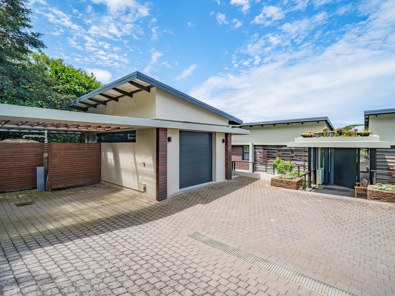 Modern front exterior featuring a paved driveway, single garage, timber pergola, and stone planter boxes leading to a covered entrance.