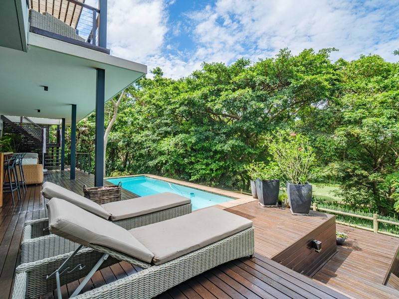 A well-maintained outdoor pool area featuring extensive timber decking, a swimming pool, and a covered patio space overlooking lush greenery.