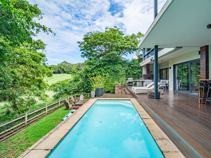 Spacious outdoor entertainment area featuring a swimming pool, timber decking, and a covered patio with a built-in braai overlooking the golf course.