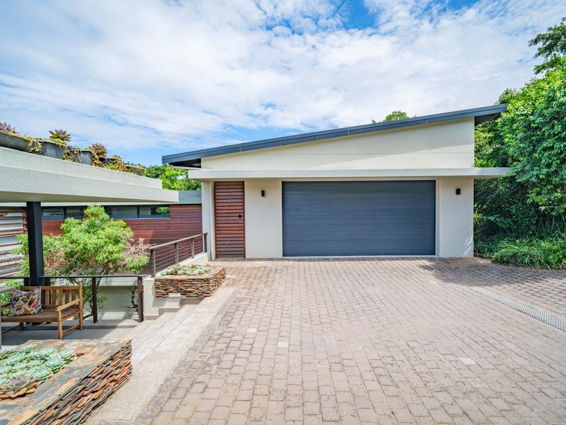 Modern front exterior featuring a paved driveway, single garage, and contemporary architectural design with timber accents and landscaped retaining walls.