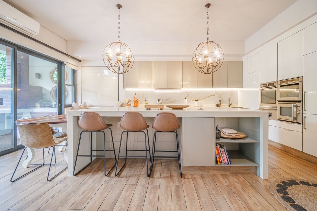 Modern kitchen featuring a large central island, integrated appliances, sleek cabinetry, and direct access to an outdoor patio area.