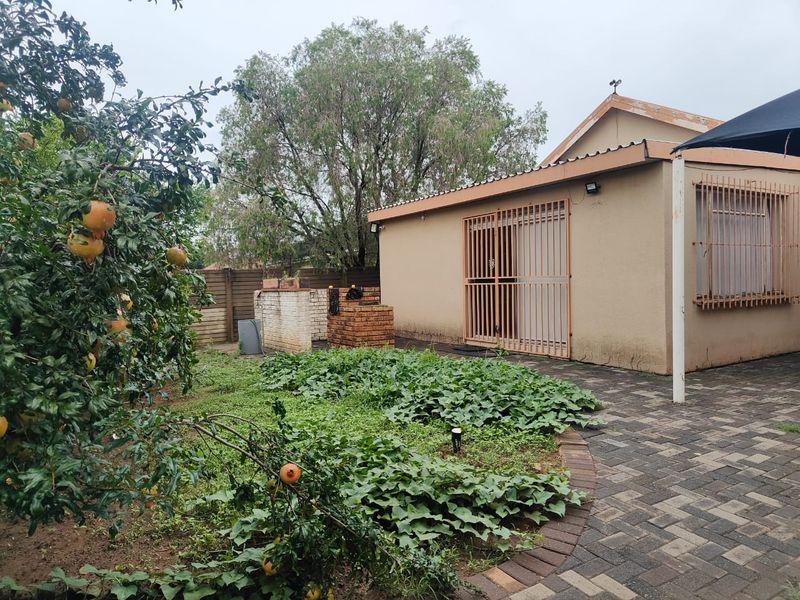 Rear exterior view showing a paved patio area, brick braai, and garden space with security features on windows and doors.