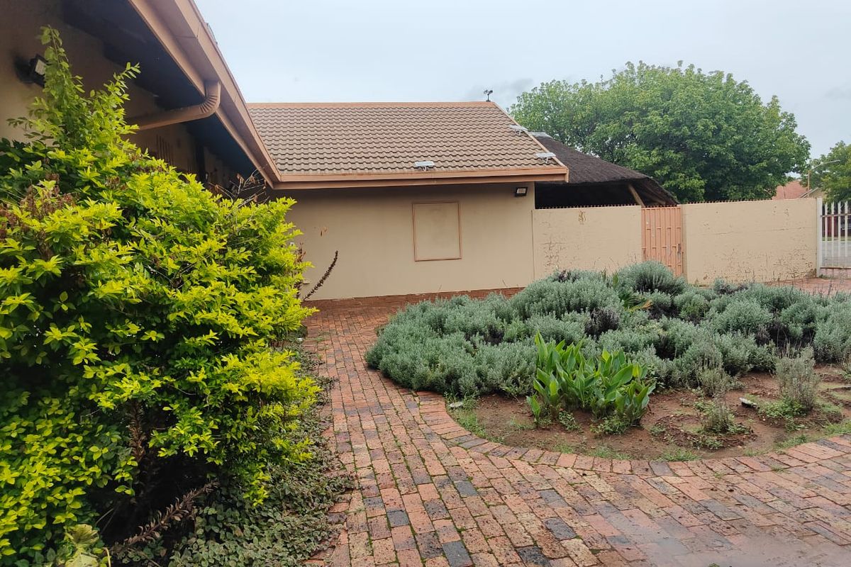 A rear exterior view featuring a brick paved pathway, landscaped garden beds, and a tiled roof structure with boundary walling.