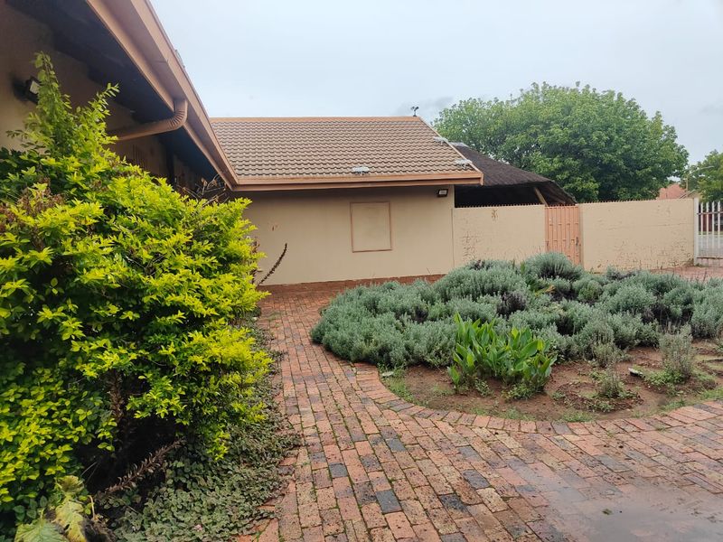 A rear exterior view featuring a brick paved pathway, landscaped garden beds, and a tiled roof structure with boundary walling.