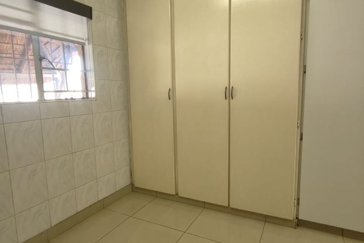 A clean, empty bedroom featuring neutral tiled flooring, tiled wall accents, and ample built-in cupboard storage space.