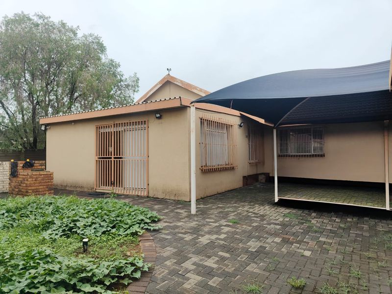 Rear exterior view featuring a paved patio area, shade sail, security features, and a built-in brick braai.