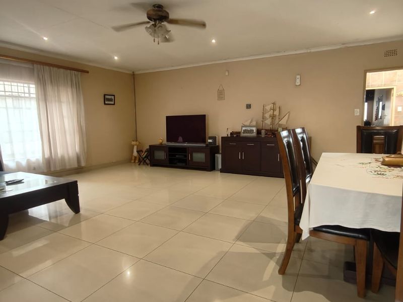 Spacious open-plan living and dining area featuring large format floor tiles, recessed downlighting, and a ceiling fan.