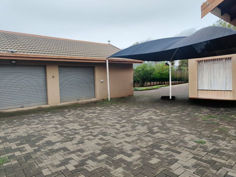 A paved driveway area featuring a double garage with roller shutter doors and a large shade sail structure.