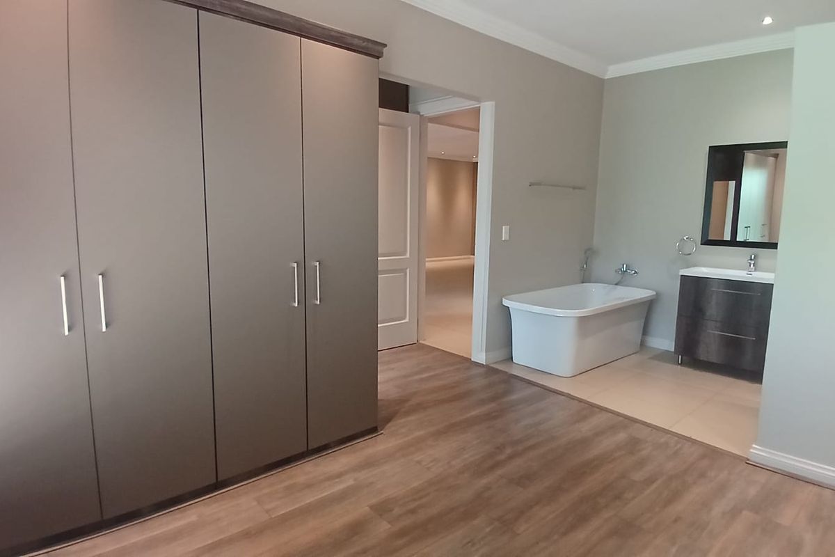 A modern bedroom featuring built-in wardrobes, wood-look flooring, and an open-plan en-suite bathroom with a freestanding bathtub and vanity.