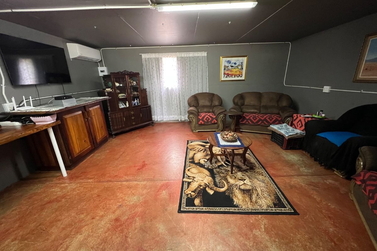 A rustic living area featuring exposed electrical conduit, painted concrete flooring, and a wall-mounted air conditioning unit.