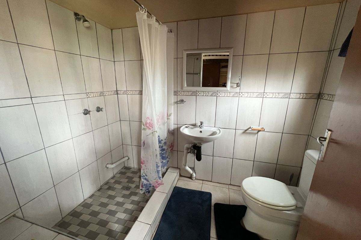 A functional bathroom featuring a walk-in shower with tiled base, wall-mounted basin, and standard toilet, finished with neutral wall tiling.