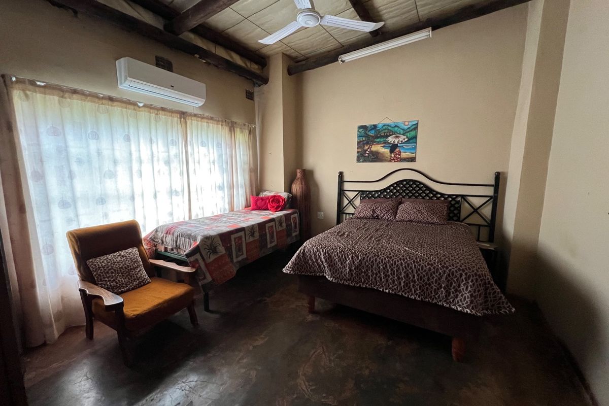 A rustic bedroom featuring exposed timber ceiling beams, a wall-mounted air conditioning unit, and polished concrete flooring.
