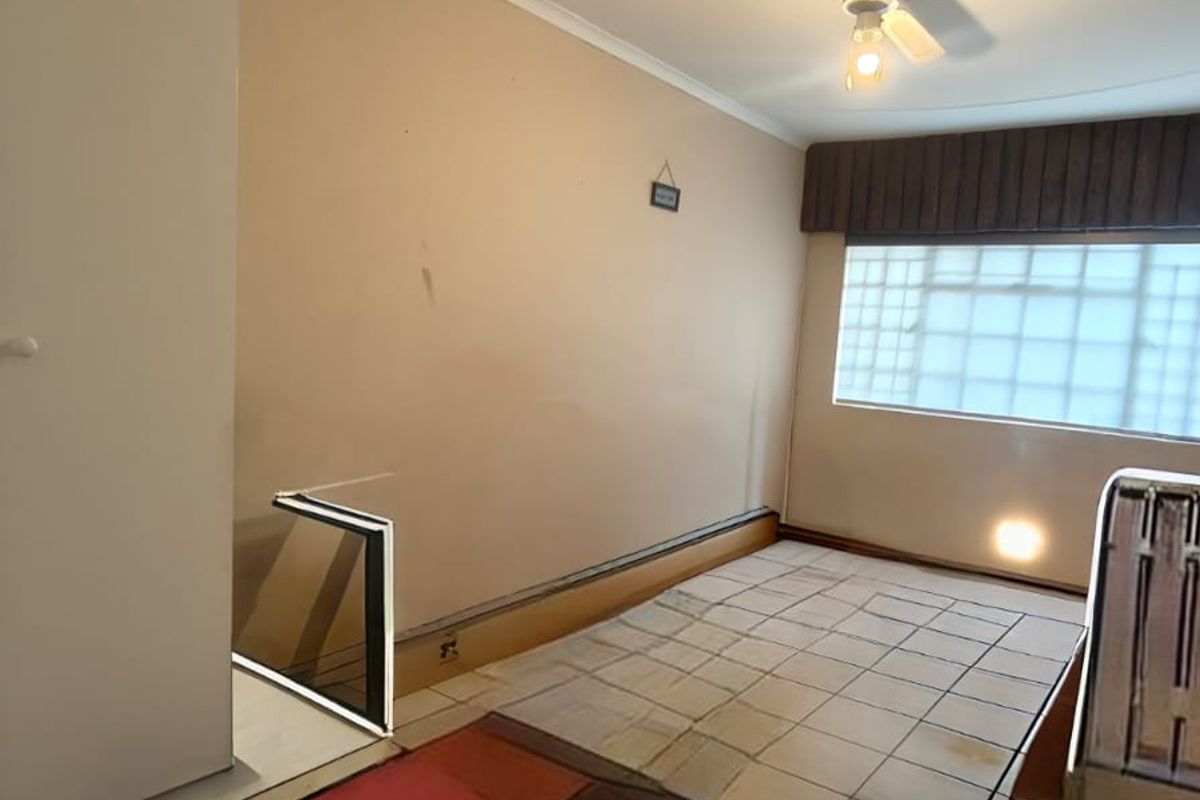 A vacant room featuring tiled flooring, a ceiling fan, and a glass block window, offering a blank canvas for potential renovation.