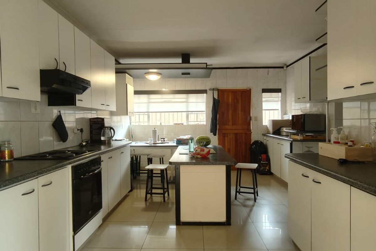 A spacious kitchen featuring white cabinetry, dark countertops, a central island, and tiled flooring, requiring some ceiling repairs.