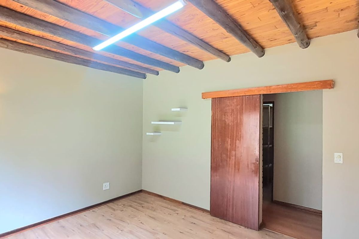 A bedroom featuring exposed timber ceiling beams, wood-look flooring, and a sliding wooden door leading to an adjacent space.