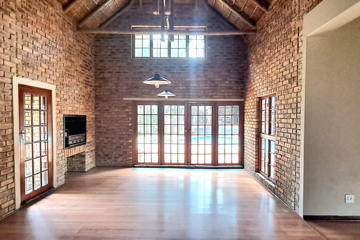 Spacious living area featuring exposed brick walls, high vaulted thatched ceiling, wooden flooring, and large glass doors leading to the outdoor pool area.