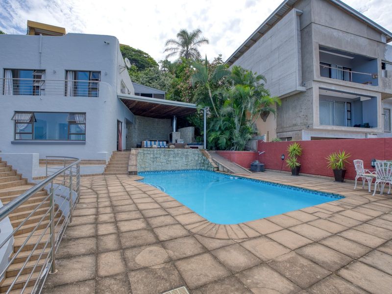 Outdoor pool area featuring a paved deck, stone feature wall, and a covered patio space, ideal for outdoor entertaining.