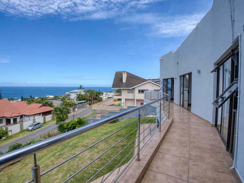Spacious elevated balcony featuring tiled flooring, stainless steel railings, and expansive ocean views, providing seamless indoor-outdoor flow through large sliding glass doors.
