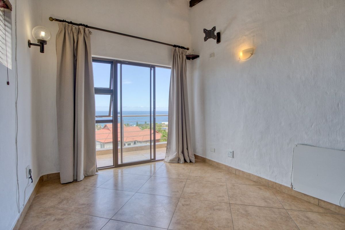 An empty bedroom featuring tiled flooring, wall-mounted lighting, and a sliding glass door that opens to a balcony with ocean views.