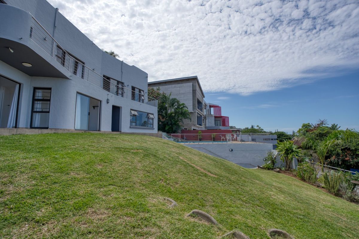 Rear view of a multi-level property featuring a sloped lawn, upper-level balconies with stainless steel balustrades, and a swimming pool area.