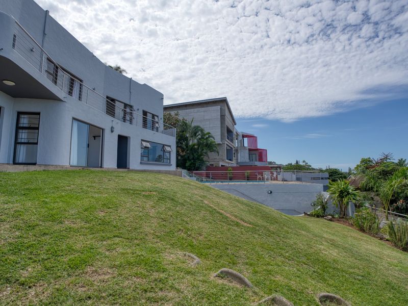 Rear view of a multi-level property featuring a sloped lawn, upper-level balconies with stainless steel balustrades, and a swimming pool area.